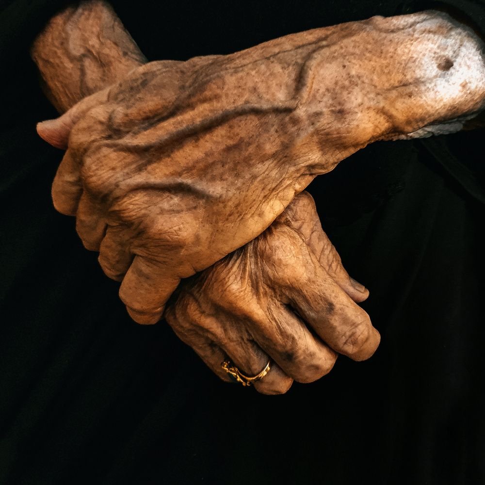 An older person's hands held gently in the hands of a caregiver.